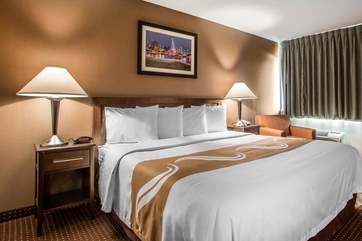 A hotel room with a large bed, two bedside tables, a chair, a framed picture on the wall, and a window with curtains.