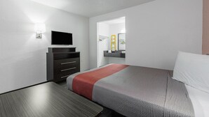 A modern hotel room with a bed, a TV on a dresser, a mirror, and a small desk.
