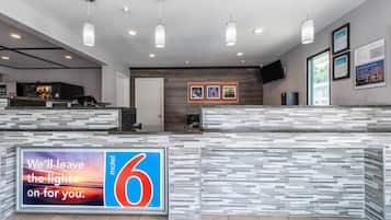 A modern hotel reception area with a large '6' sign, a digital screen displaying a sunset, and a counter with a tiled backsplash.