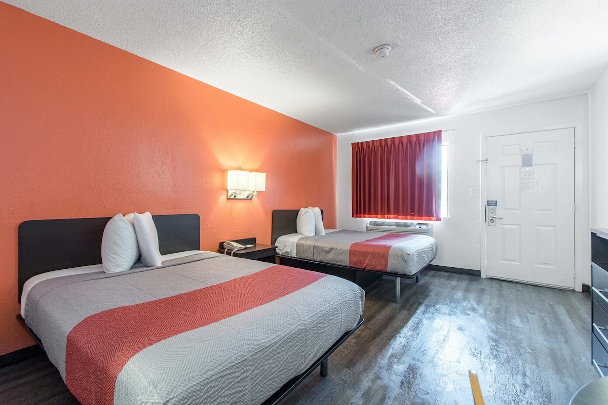 A hotel room with two beds, a red curtain, a white door, and a wall-mounted lamp.