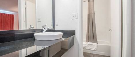 Un baño con lavamanos blanco, encimera negra y cortina de ducha.
