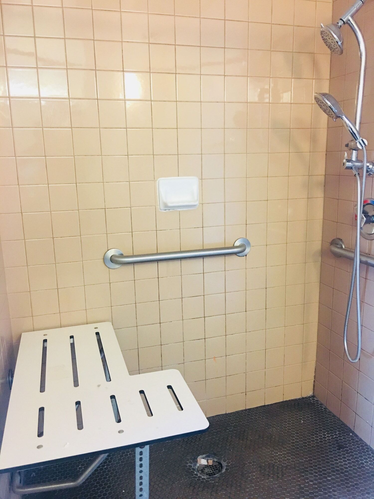 Un petit espace de douche carrelé, équipé d’une barre d’appui et d’un lavabo blanc.