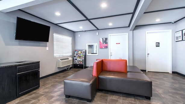 A lobby with a sectional sofa, a flat-screen TV, a magazine rack, and a reception desk. - Motel 6 Norcross, GA - Atlanta Northeast (Norcross)