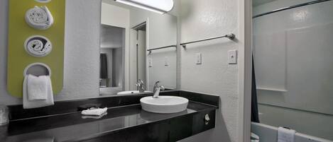 Un baño moderno con encimera negra, lavabo blanco y un espejo grande. Se observan tres sujetahierbas en la pared y un box de ducha de vidrio.