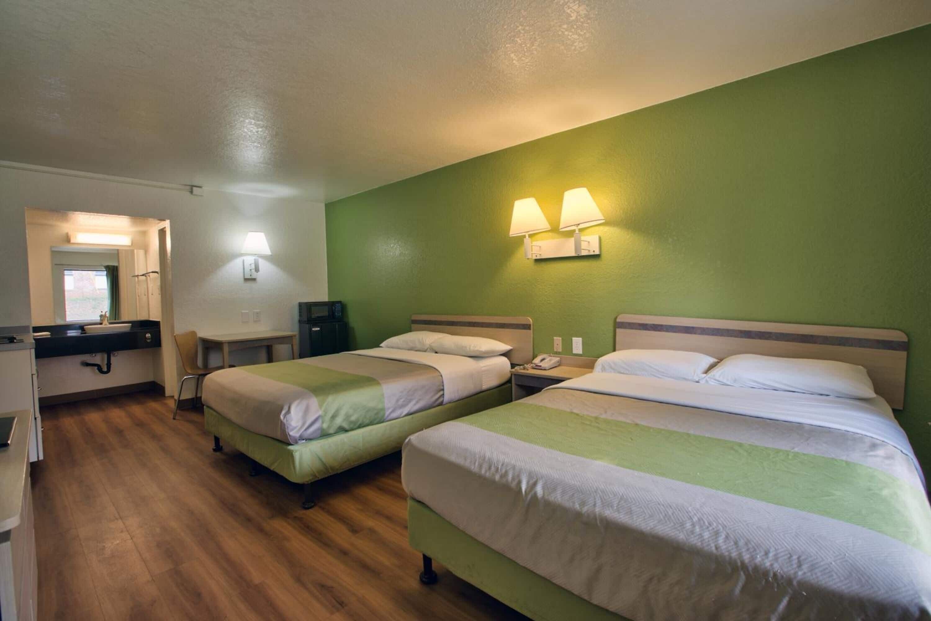 A hotel room with two beds, a desk, and a chair. There are two wall-mounted lamps and a telephone on the nightstand.