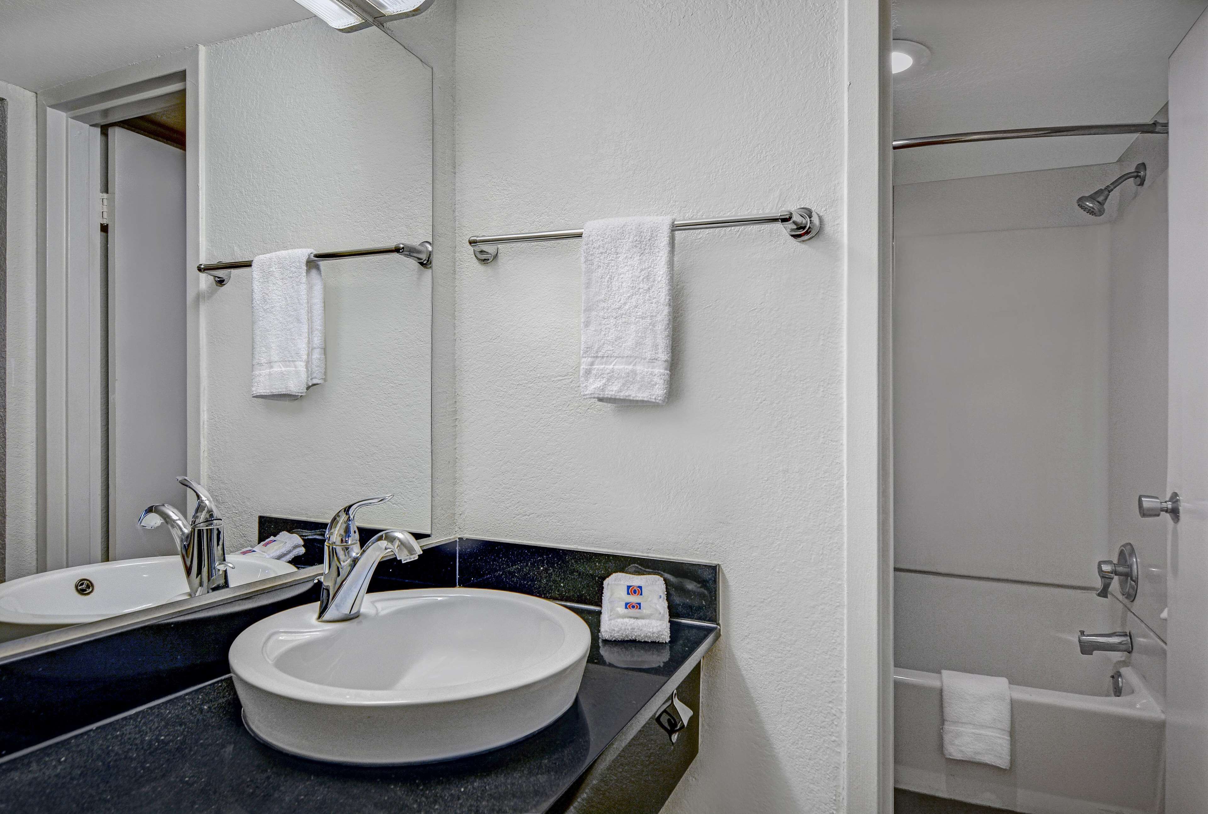 A bathroom with a round sink, two towel bars with white towels, a mirror, and a shower area.
