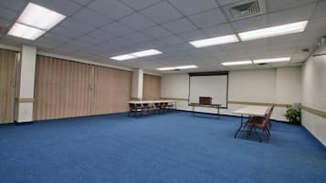 Une grande salle de conférence dotée d’un tapis bleu, d’un tableau blanc et d’un écran de projection.