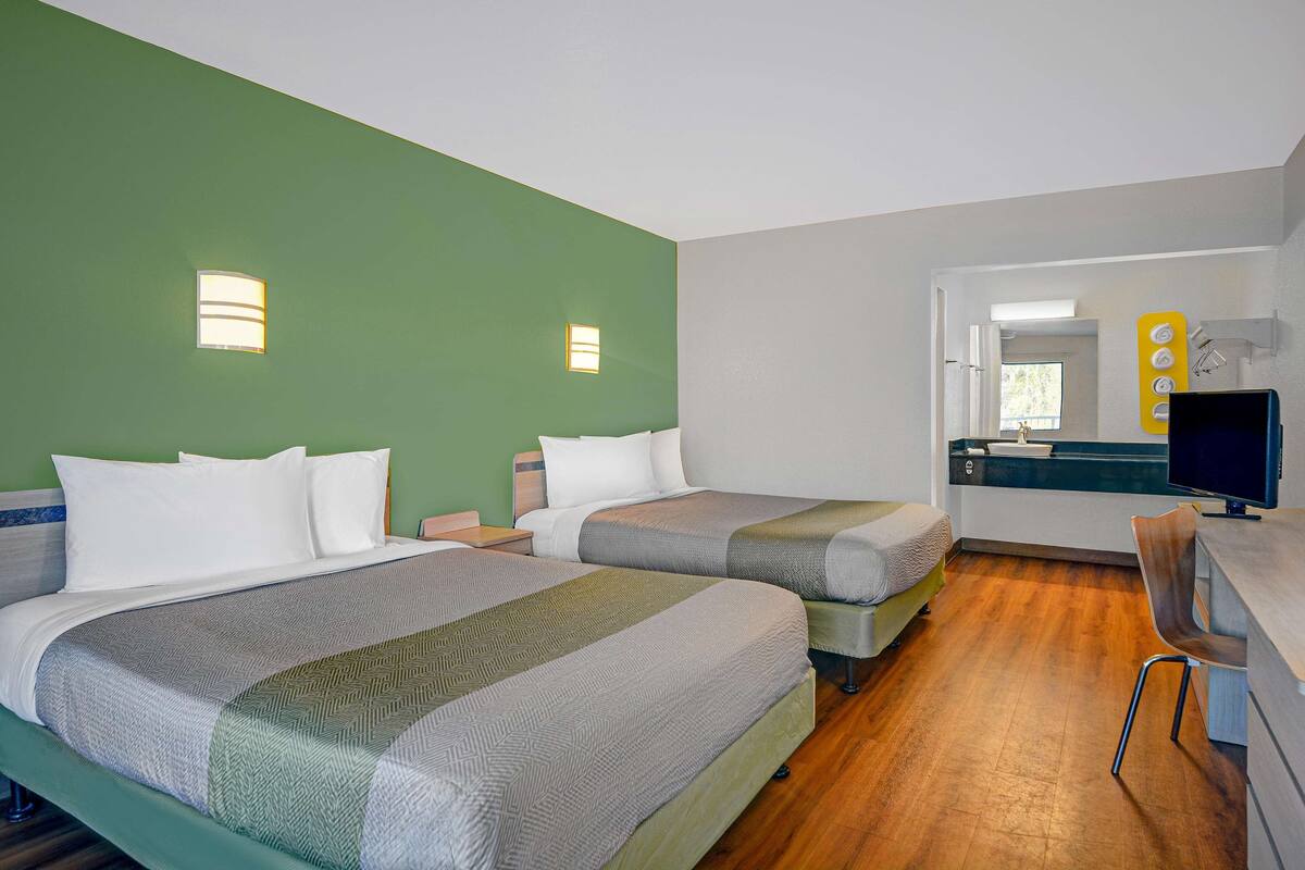 A hotel room with two beds, a desk with a computer, and a bathroom visible through an open door.