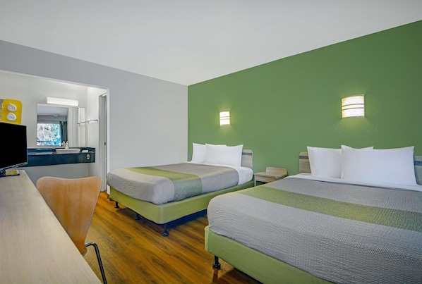 A hotel room with two beds, a desk, a chair, and a bathroom visible through an open door.