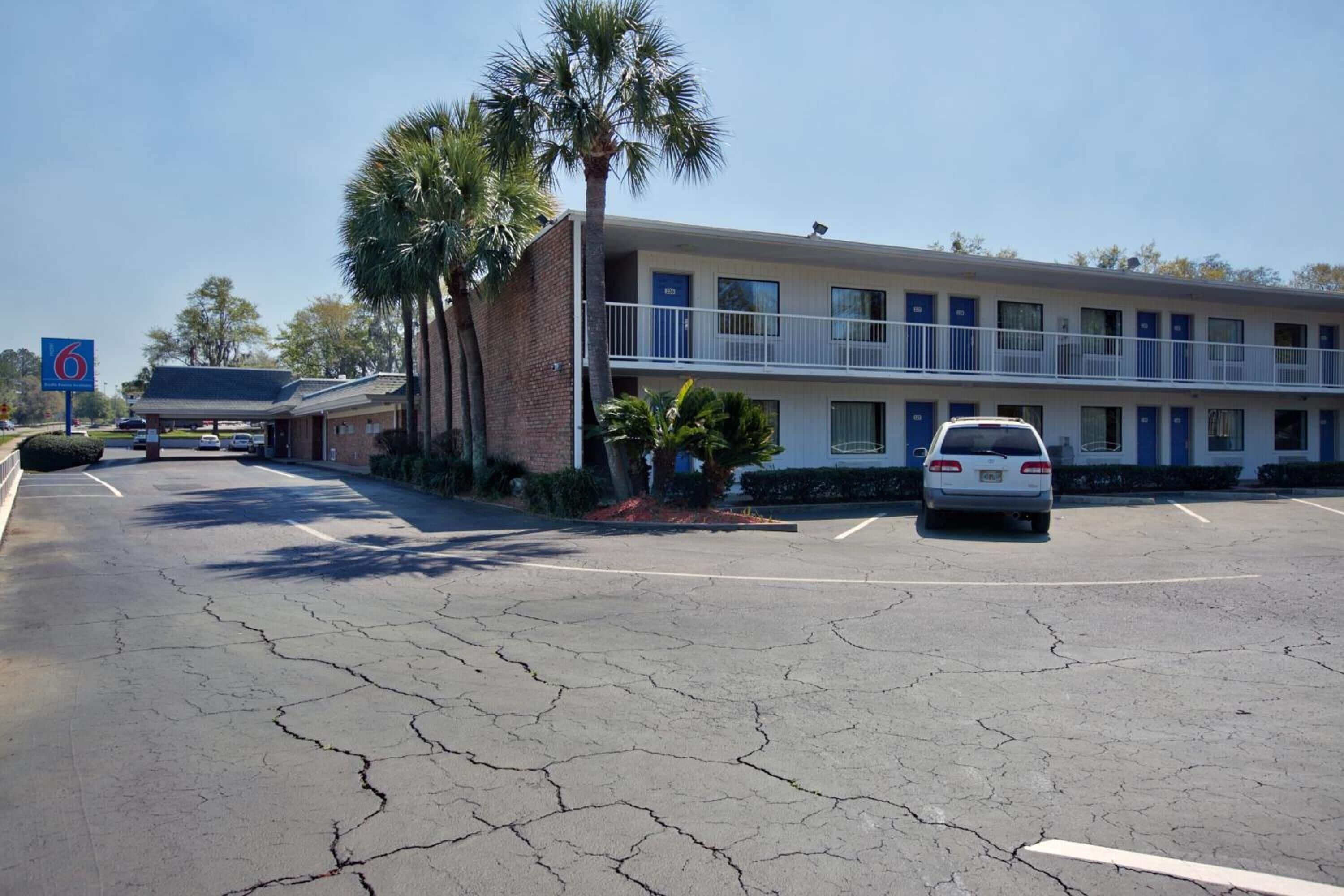 A motel with a two-story structure, a parking lot, and a palm tree.