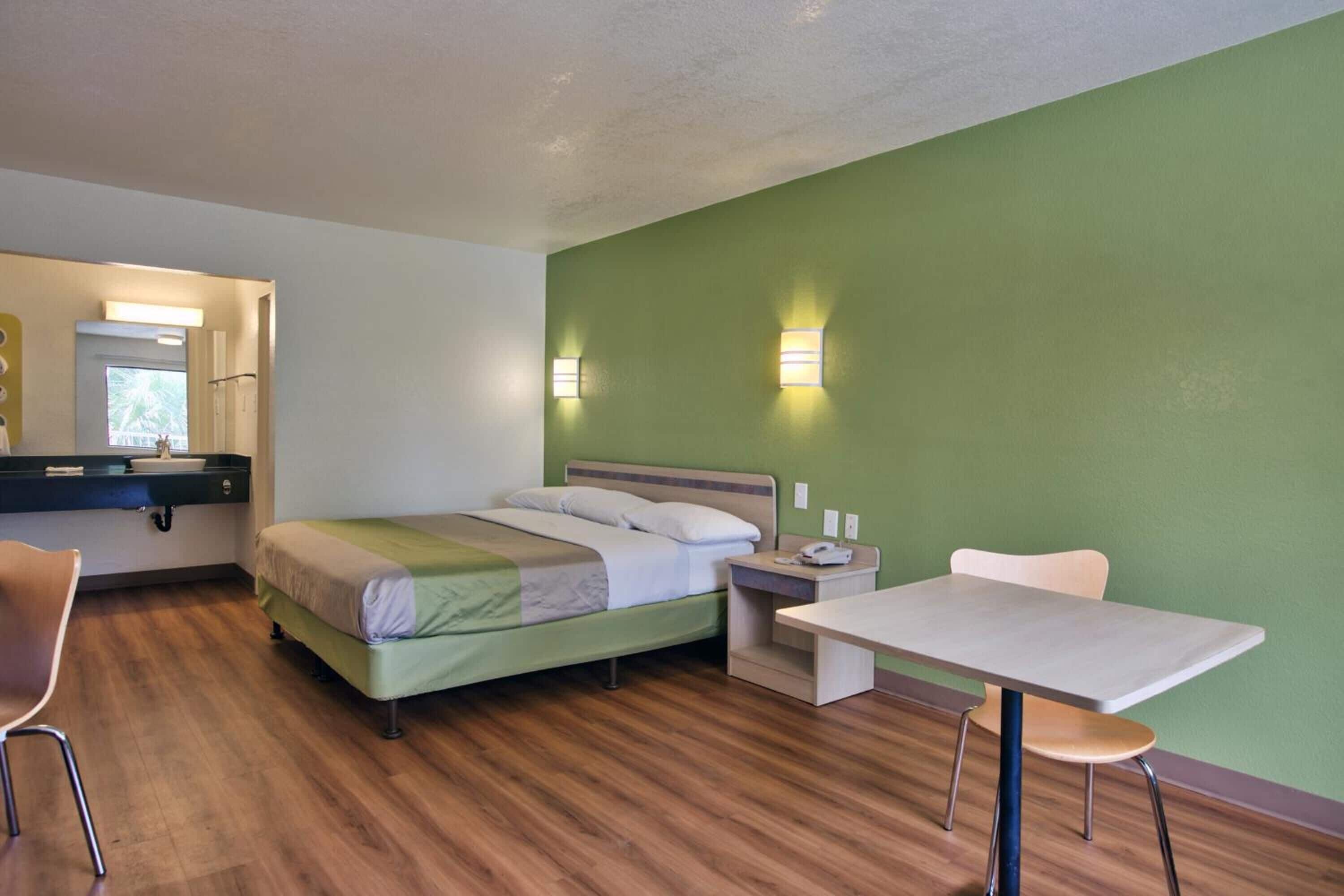 A hotel room with a bed, a desk, a chair, a nightstand, and a mirror.