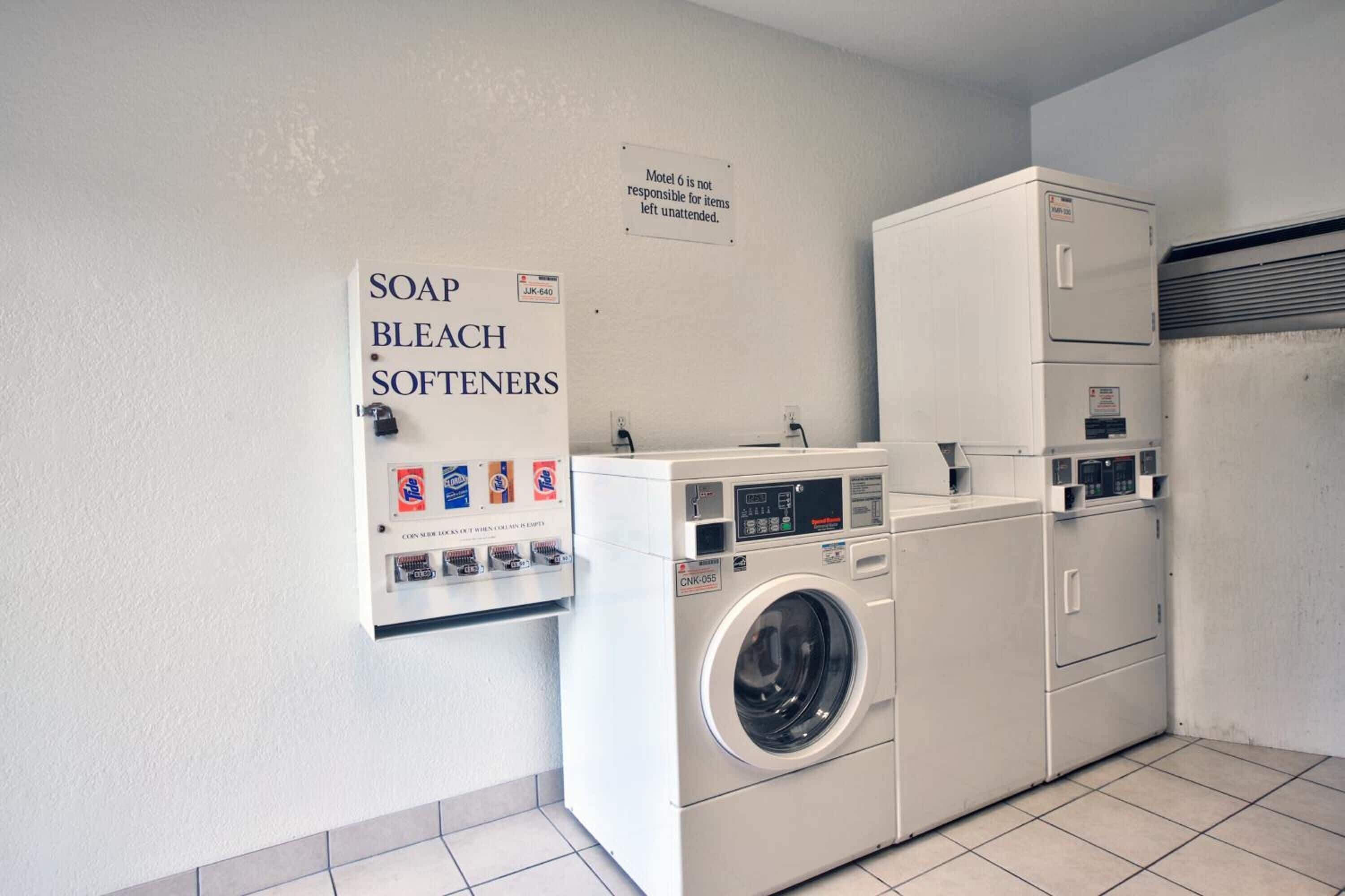 A laundry area with a washing machine, dryer, and a sign indicating soap, bleach, and softeners available.