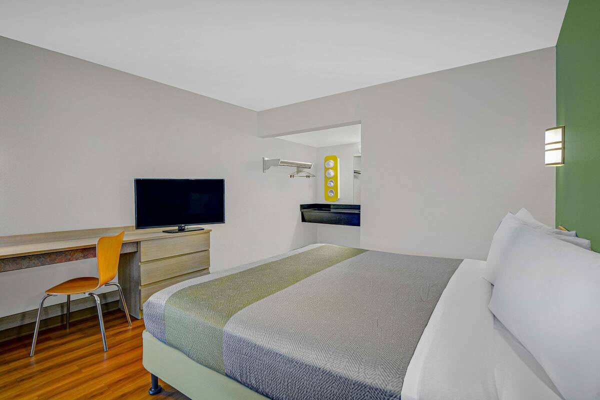 A hotel room with a bed, a desk, a chair, a television, and a mirror.
