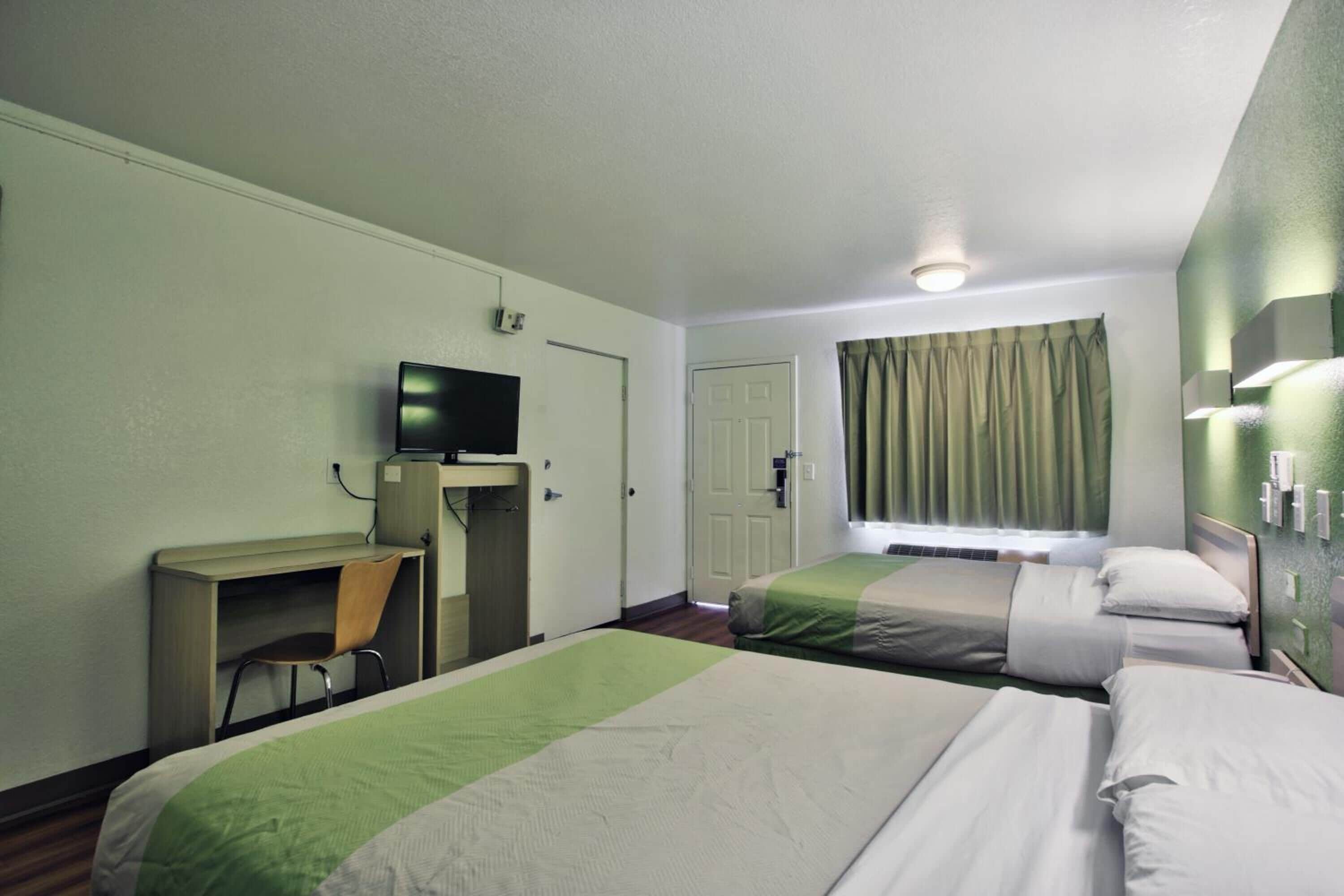 Habitación de hotel con dos camas, un escritorio, un televisor y una ventana con cortinas.