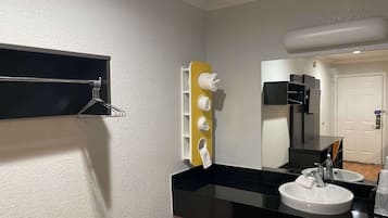 A bathroom with a black countertop, white sink, and a mirror. There is a towel rack on the wall and a toilet paper holder.