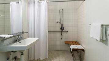 Een badkamer met een witte wastafel, een douche met glazen deur, een bankje en een handdoekrek.
