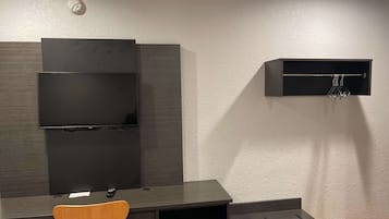 Quarto moderno com televisão de tela plana na parede, uma pequena prateleira com ganchos, uma mesa com cadeira e piso de madeira.