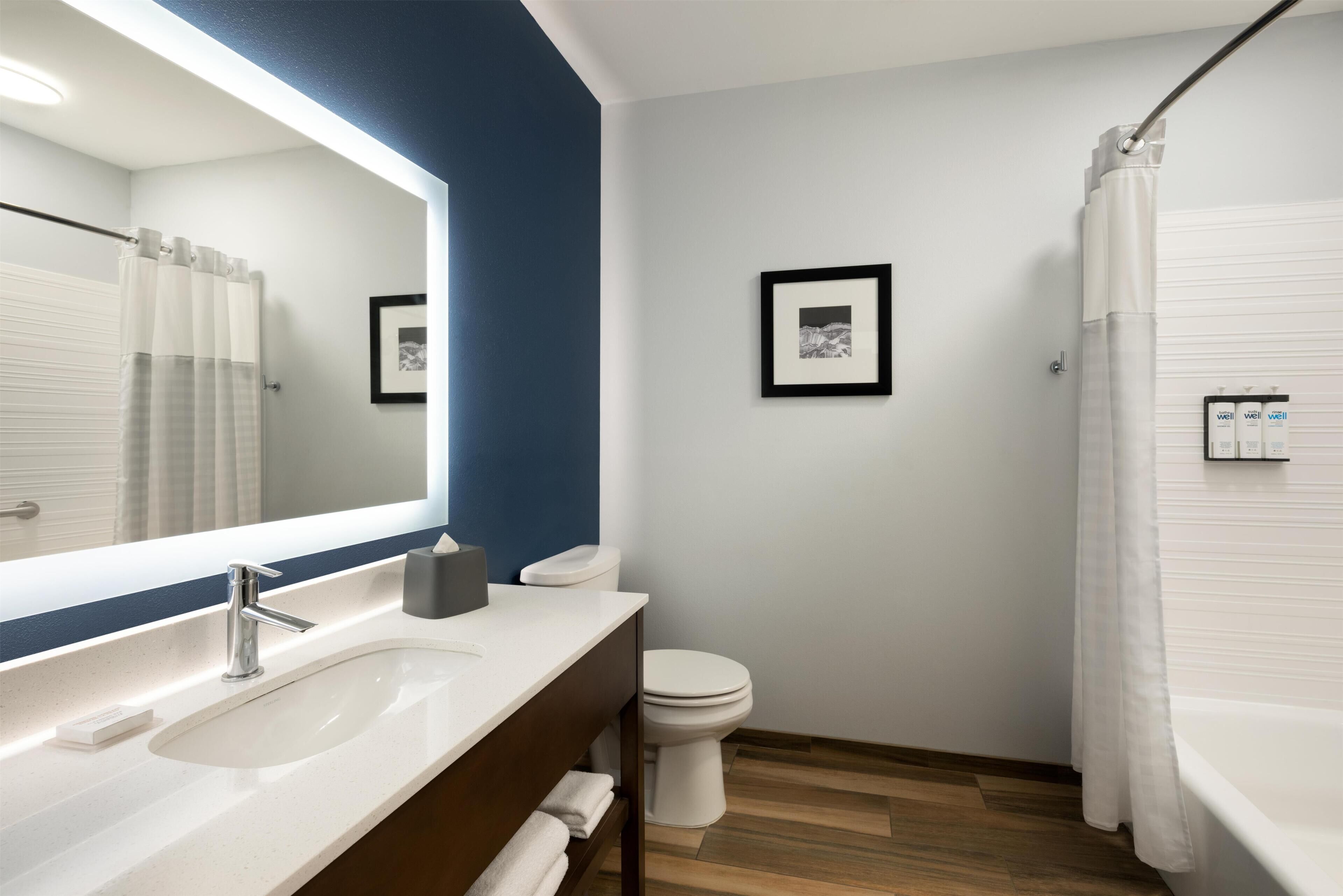 Un baño moderno con un lavamanos blanco, un espejo, un inodoro y una cortina de ducha.