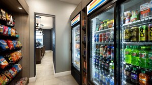 Un pasillo con bolsas de bocadillos, un refrigerador lleno de Mountain Dew y vista a una habitación con ventilador de techo.