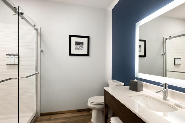 Une salle de bain moderne avec des toilettes blanches, un grand miroir, un lavabo blanc et une douche avec des portes en verre.