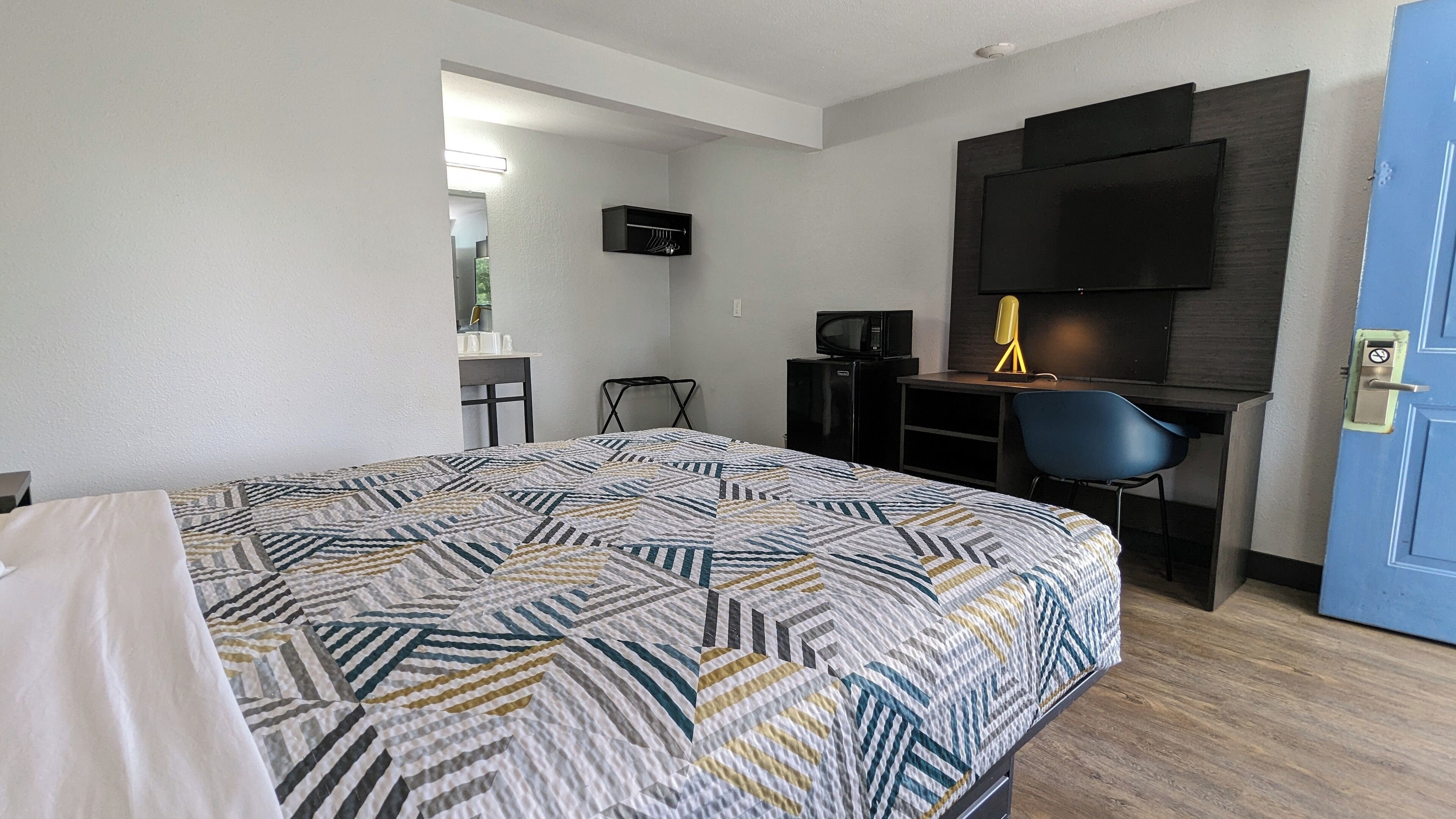 A hotel room with a bed, a desk with a chair, a TV, and a door.