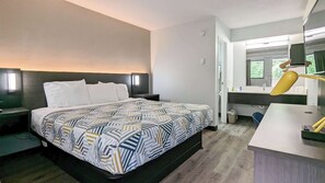 A modern hotel room with a large bed, bedside tables, a desk with a lamp, a mirror, and a window with a view of greenery. - Motel 6 Nashua, NH - North (Nashua)