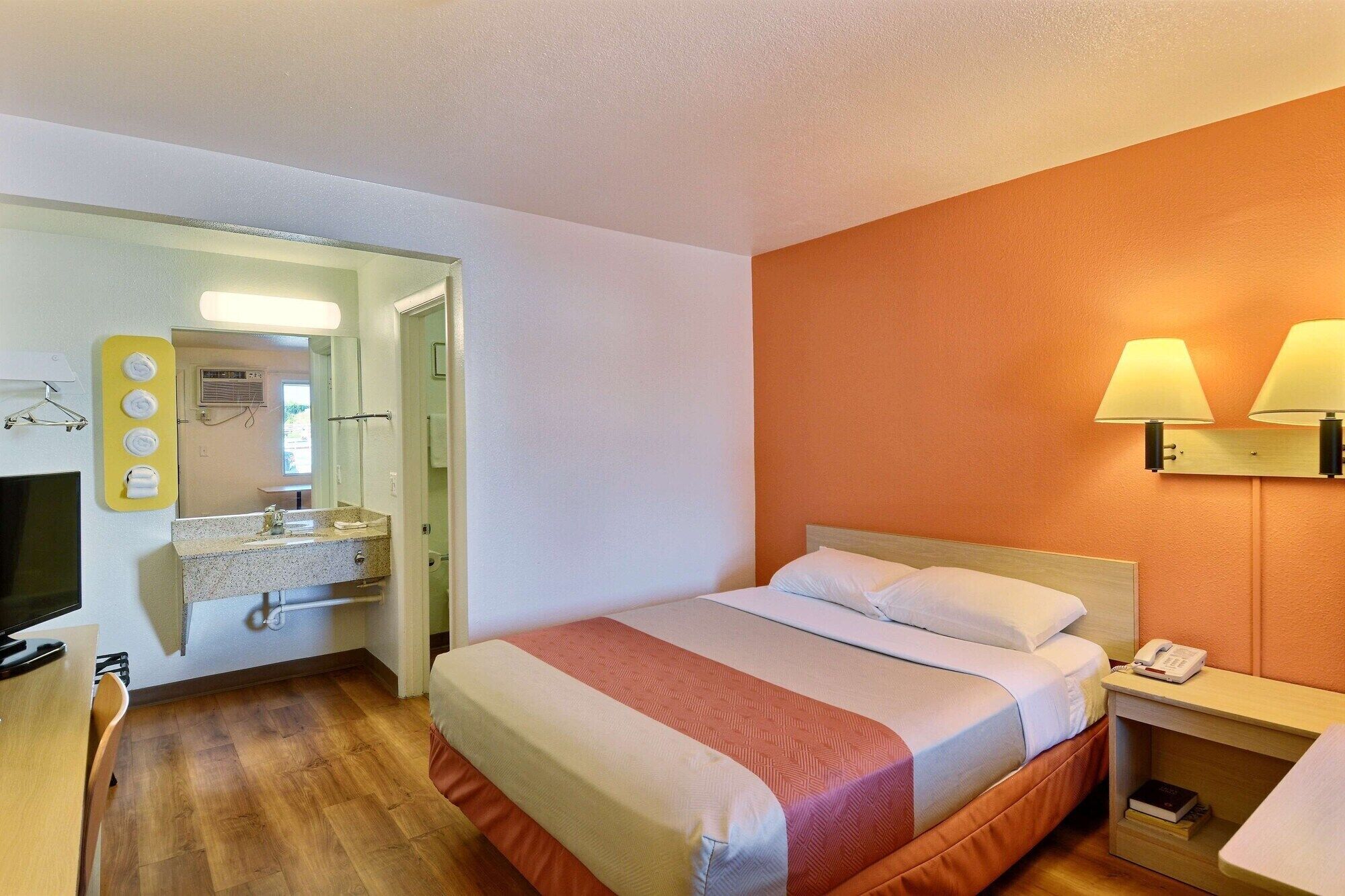 A hotel room with a bed, bedside table, lamp, and a TV.