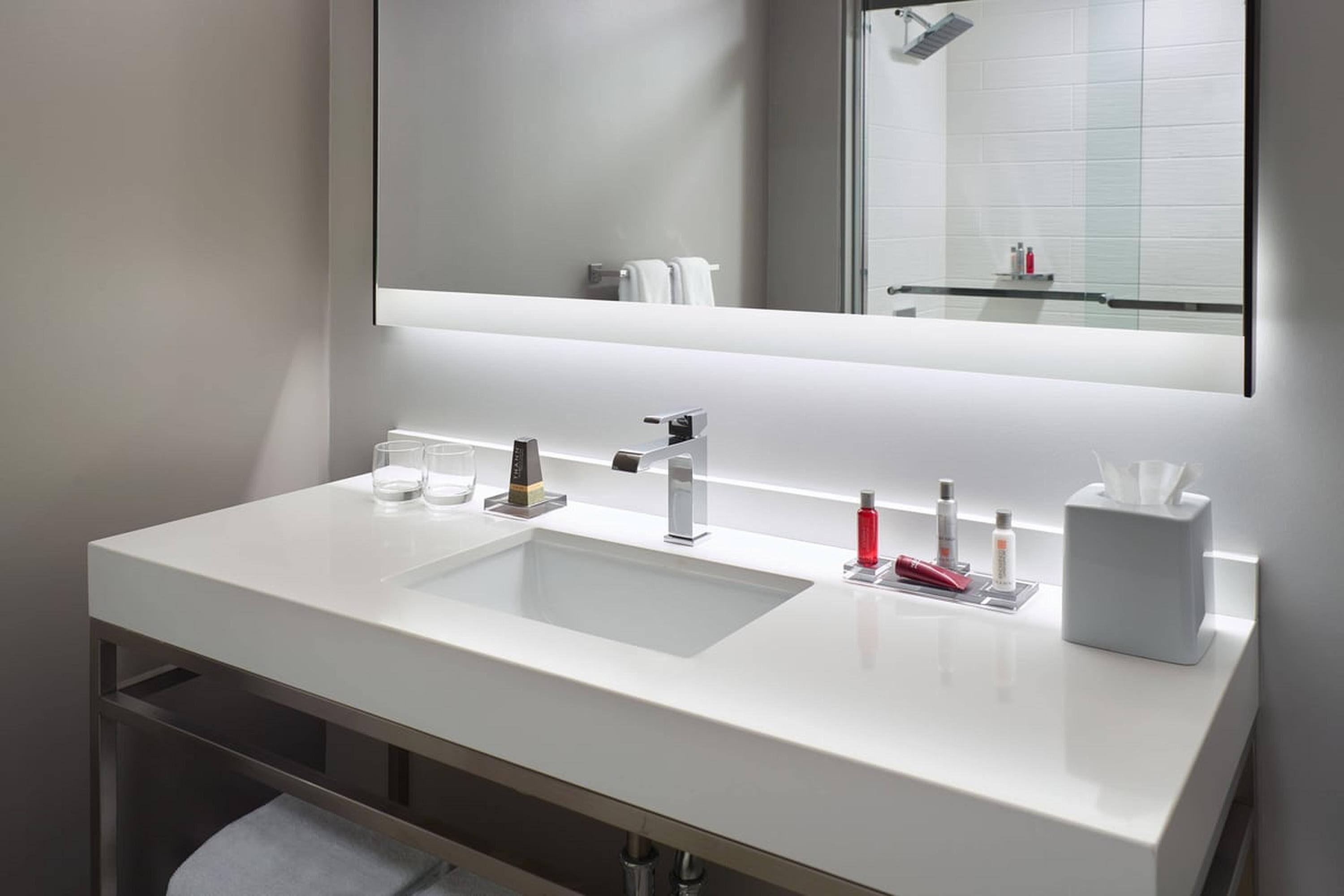 A modern bathroom with a white sink, two faucets, a mirror, and a towel rack.