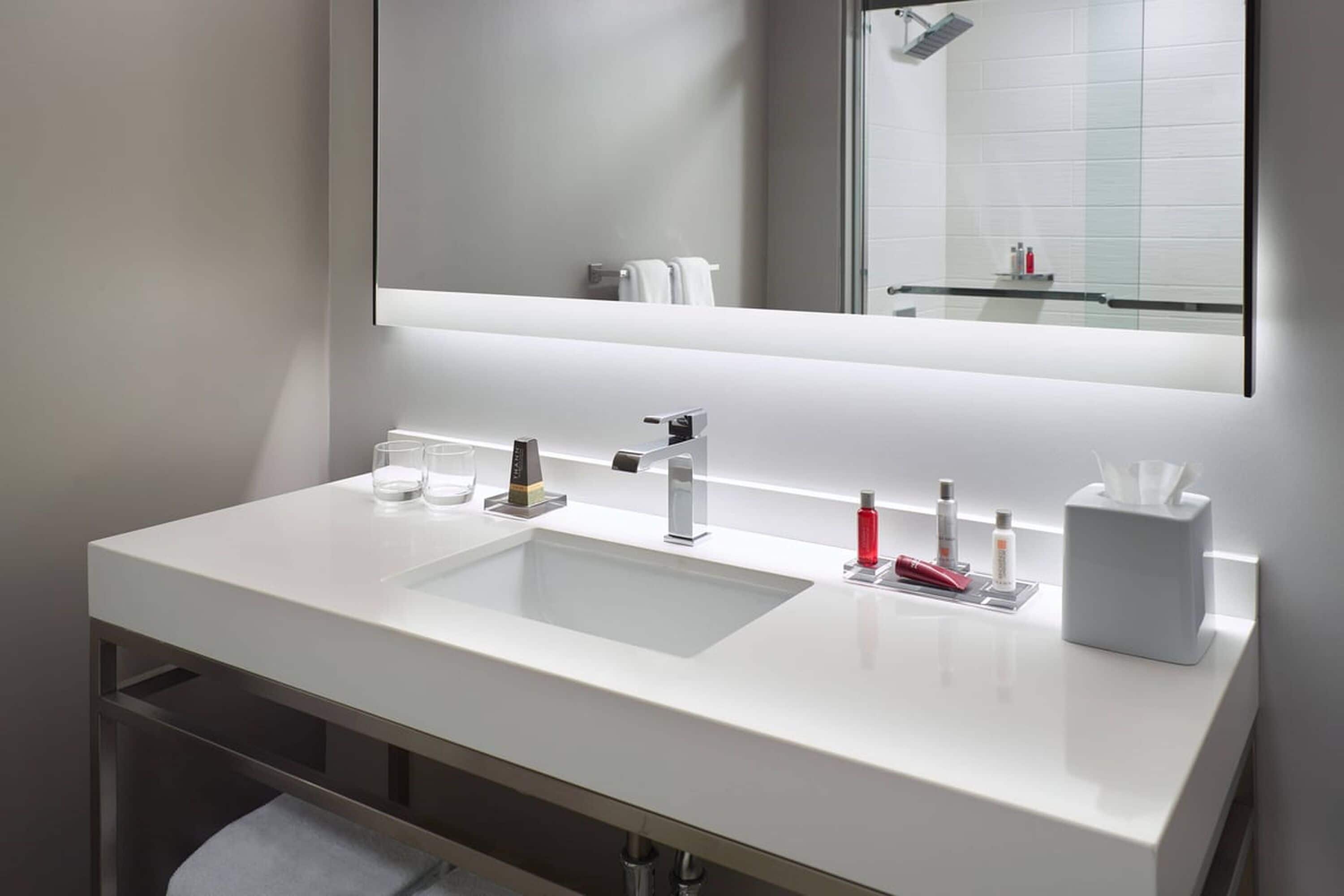 Une salle de bain moderne avec un lavabo blanc, deux robinets et un grand miroir au-dessus du lavabo.