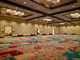 Un amplio salón de conferencias con alfombra estampada, varias puertas y luces en el techo.