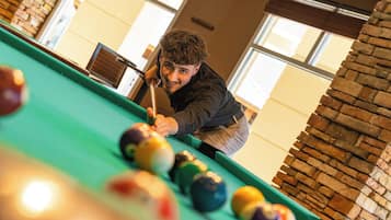 Eine Person spielt Billard in einem Raum mit Ziegelwand und großen Fenstern.