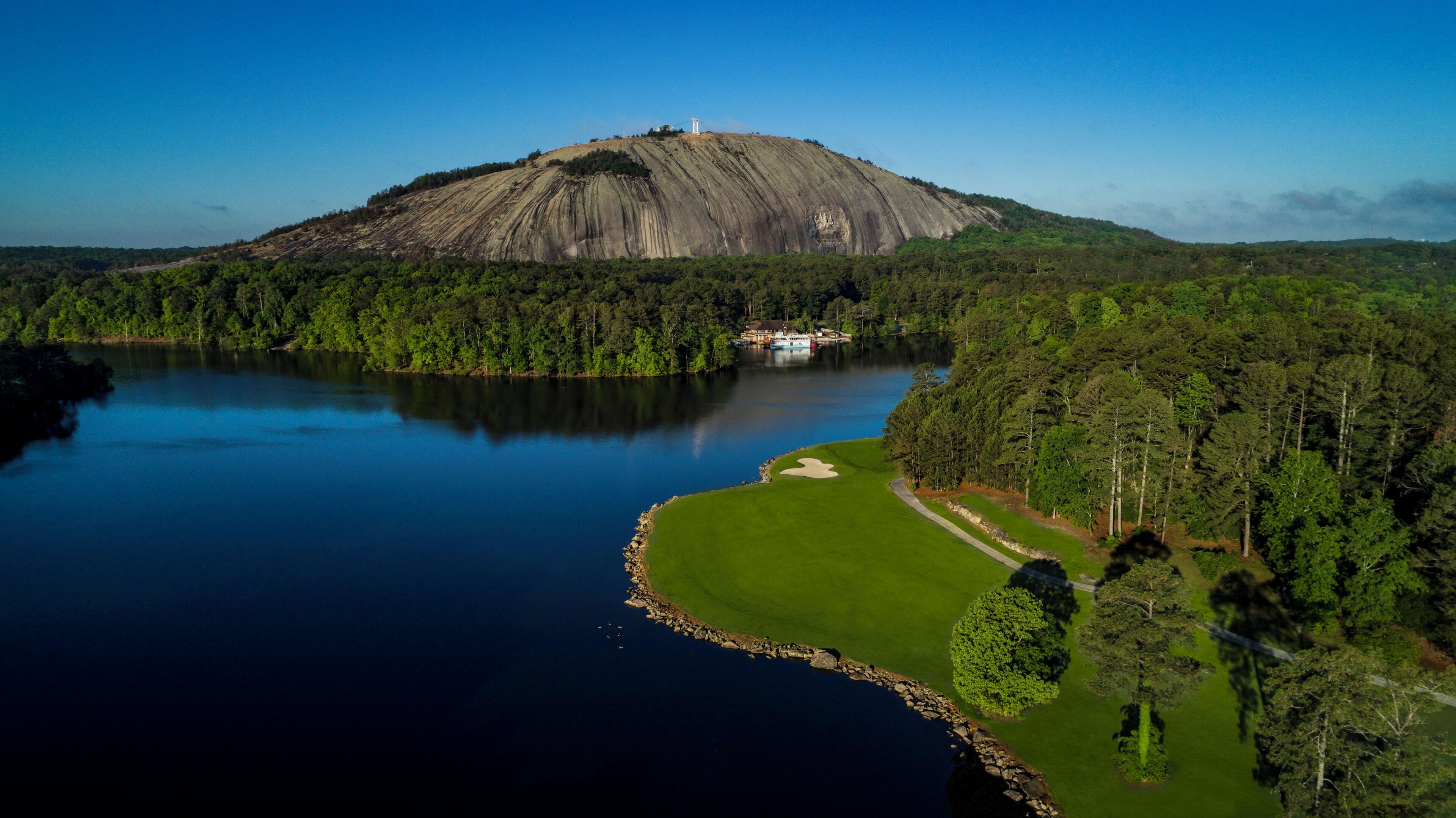 Suuri vuori, jonka huipulla on pieni rakennus, ja vuoren ympärillä on tiheää metsää ja järvi.