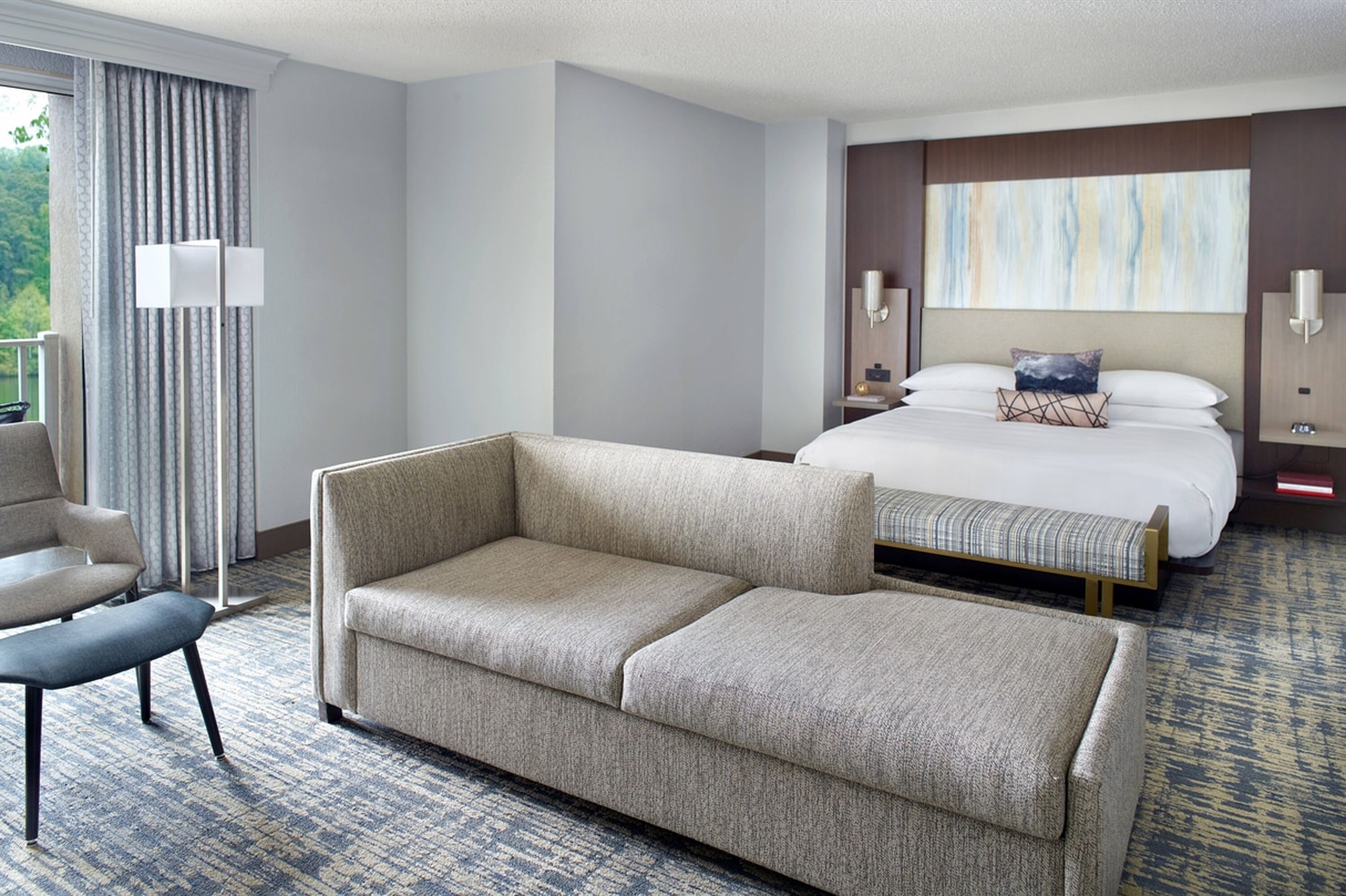 A hotel room with a large bed, a sofa, a chair, and a floor lamp.