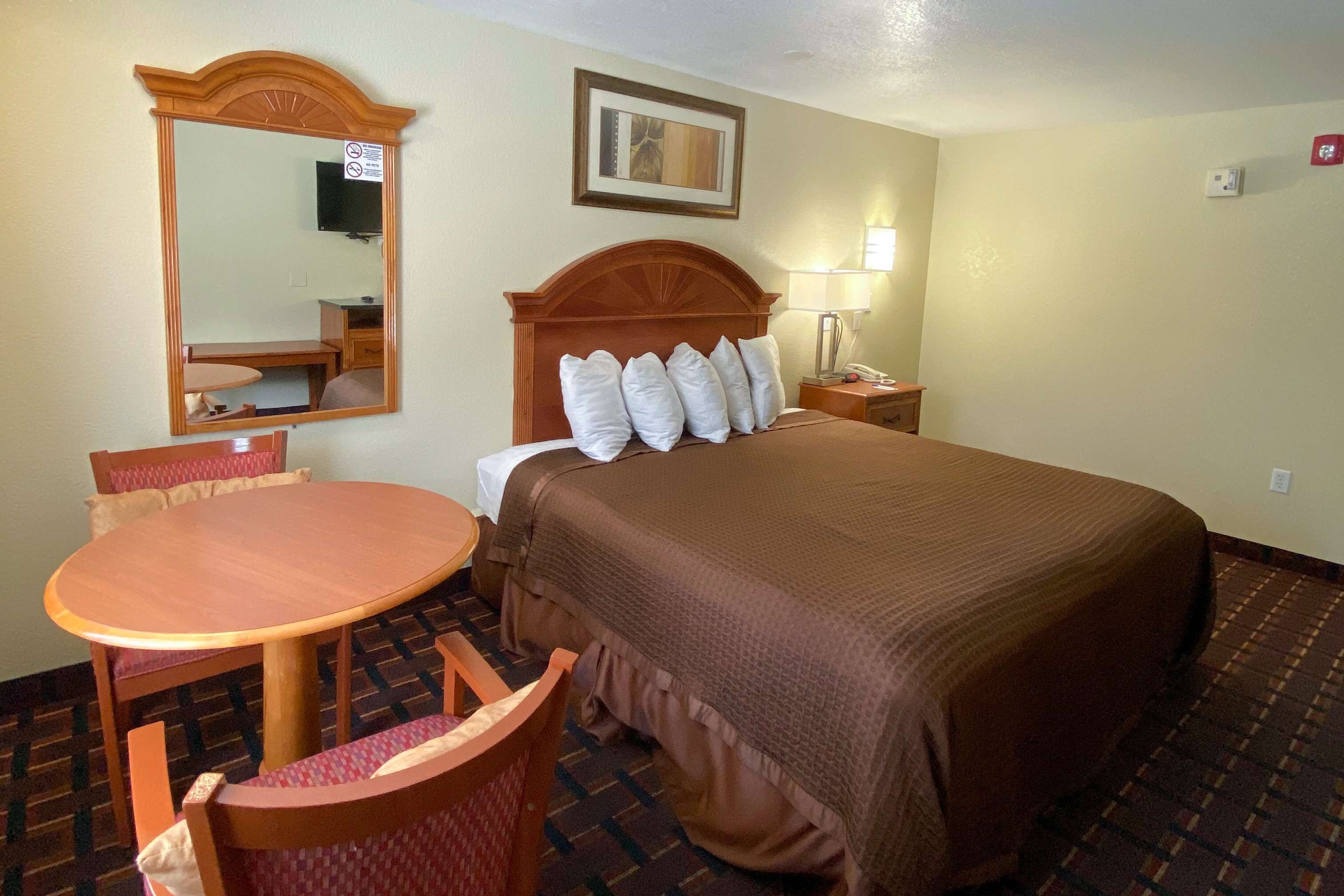 Una habitación de hotel con cama, escritorio, silla, espejo y televisor.