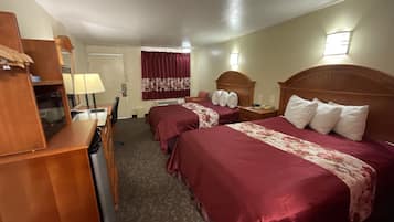 Habitación de hotel con dos camas, un escritorio, una silla, un armario y un ventanal con cortinas.