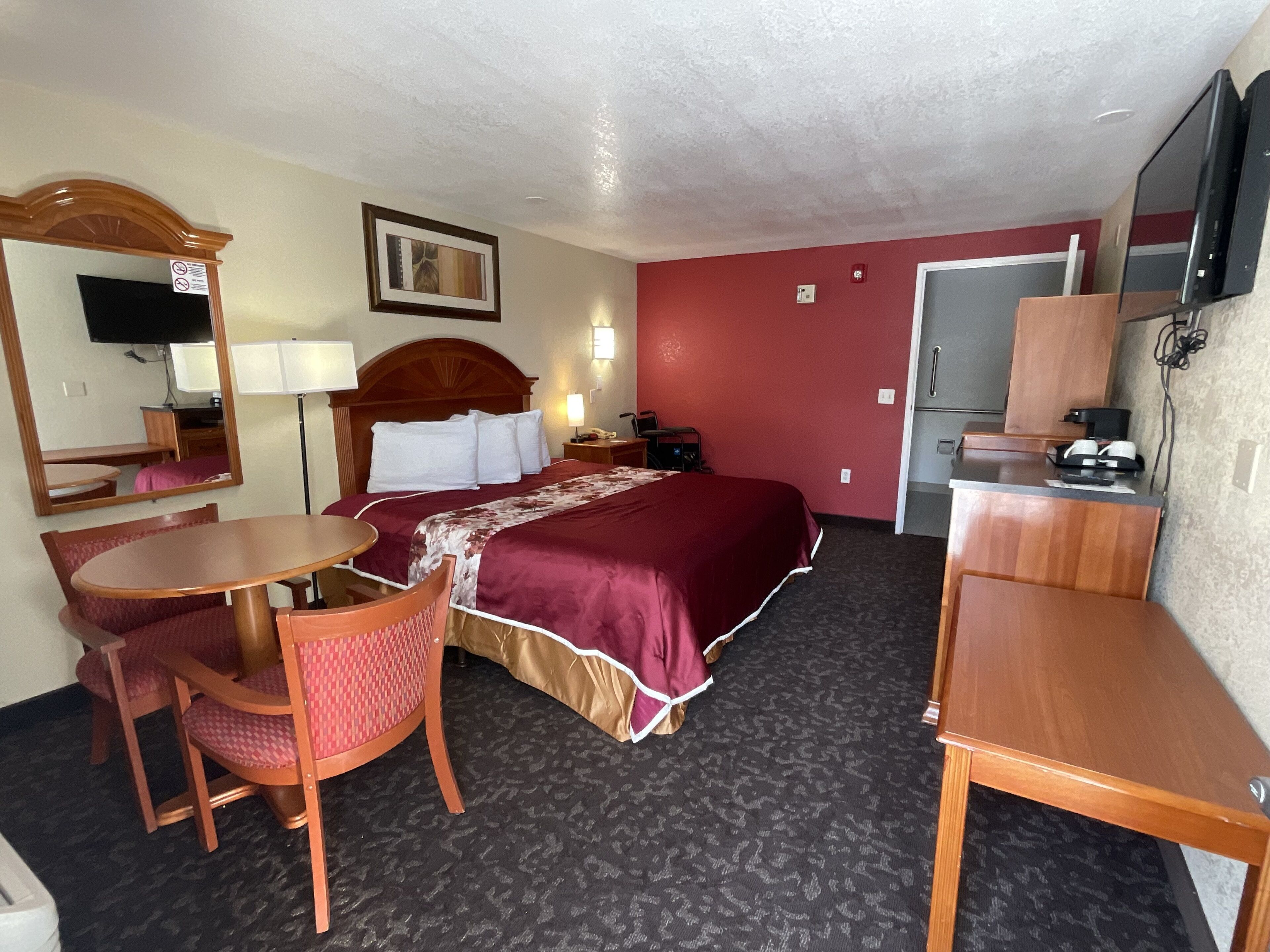 A hotel room with a bed, a desk, a chair, a TV, and a mirror.