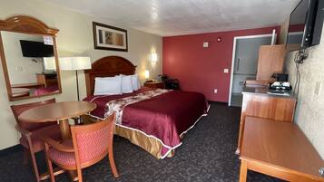 A hotel room with a bed, a desk, a chair, a TV, and a mirror.