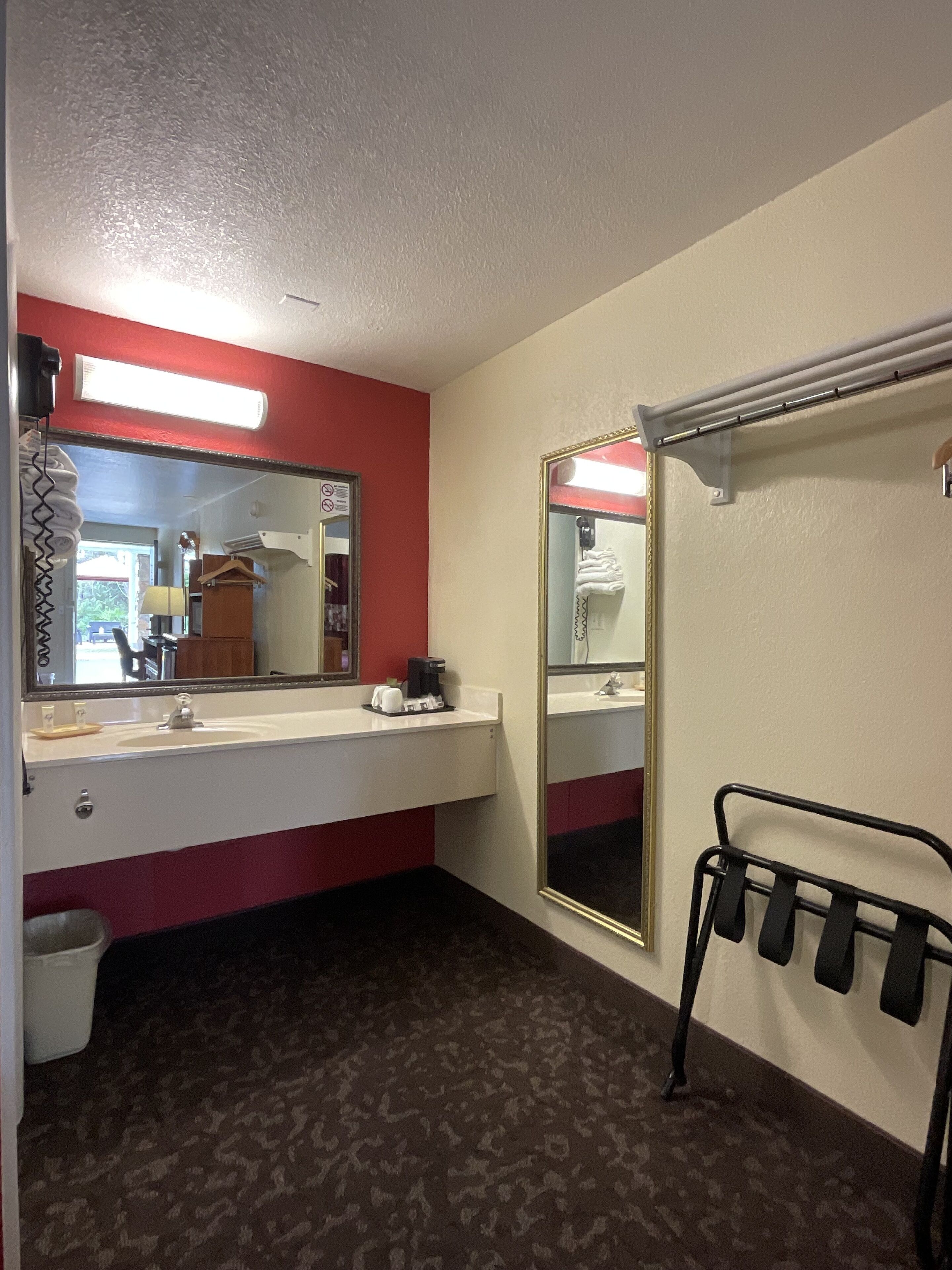 Un baño de hotel con un lavamanos blanco, paredes rojas, un espejo grande, un perchero para toallas y una zona de ducha.
