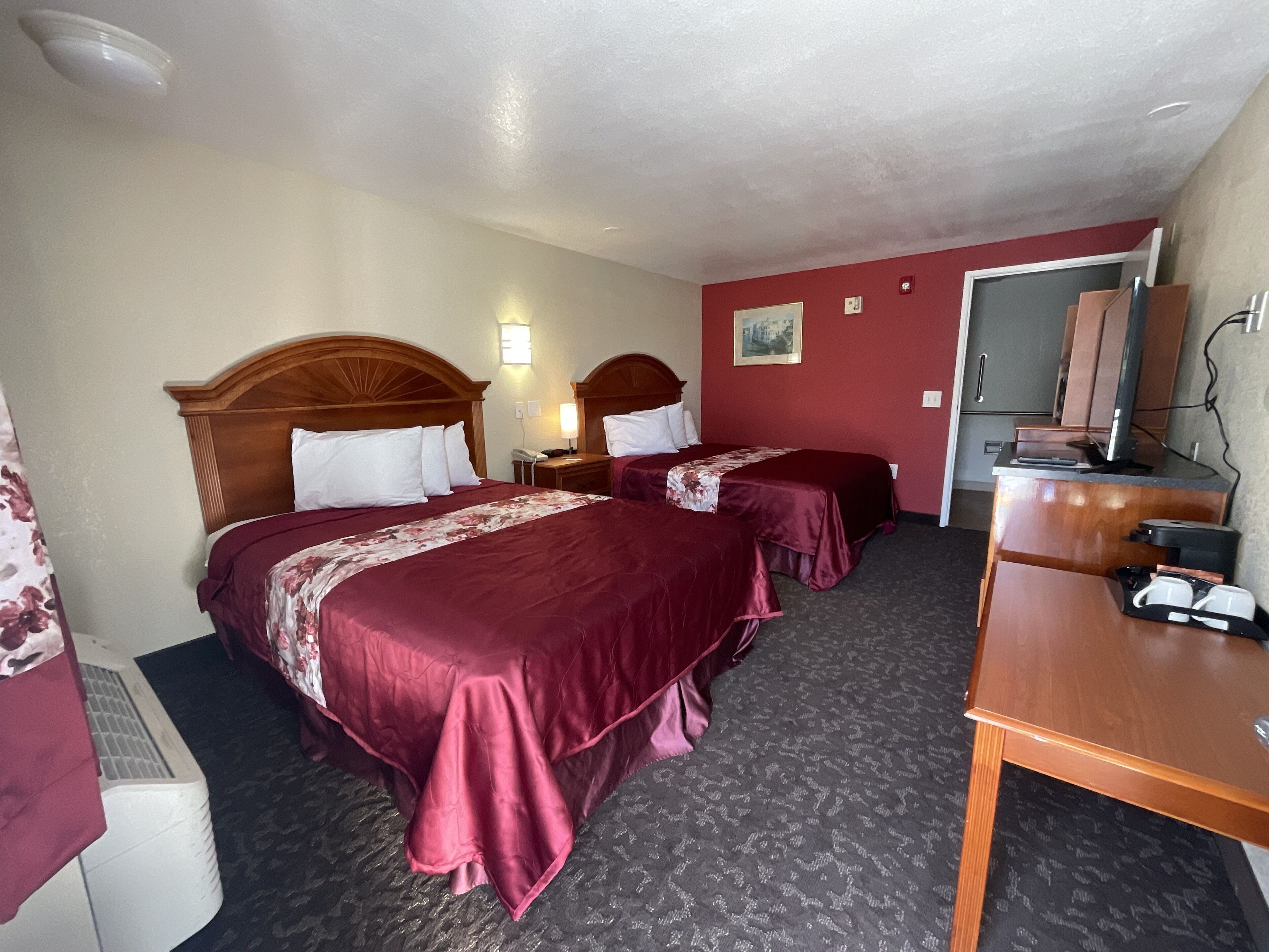 A hotel room with two beds, a desk, a mirror, and a telephone.