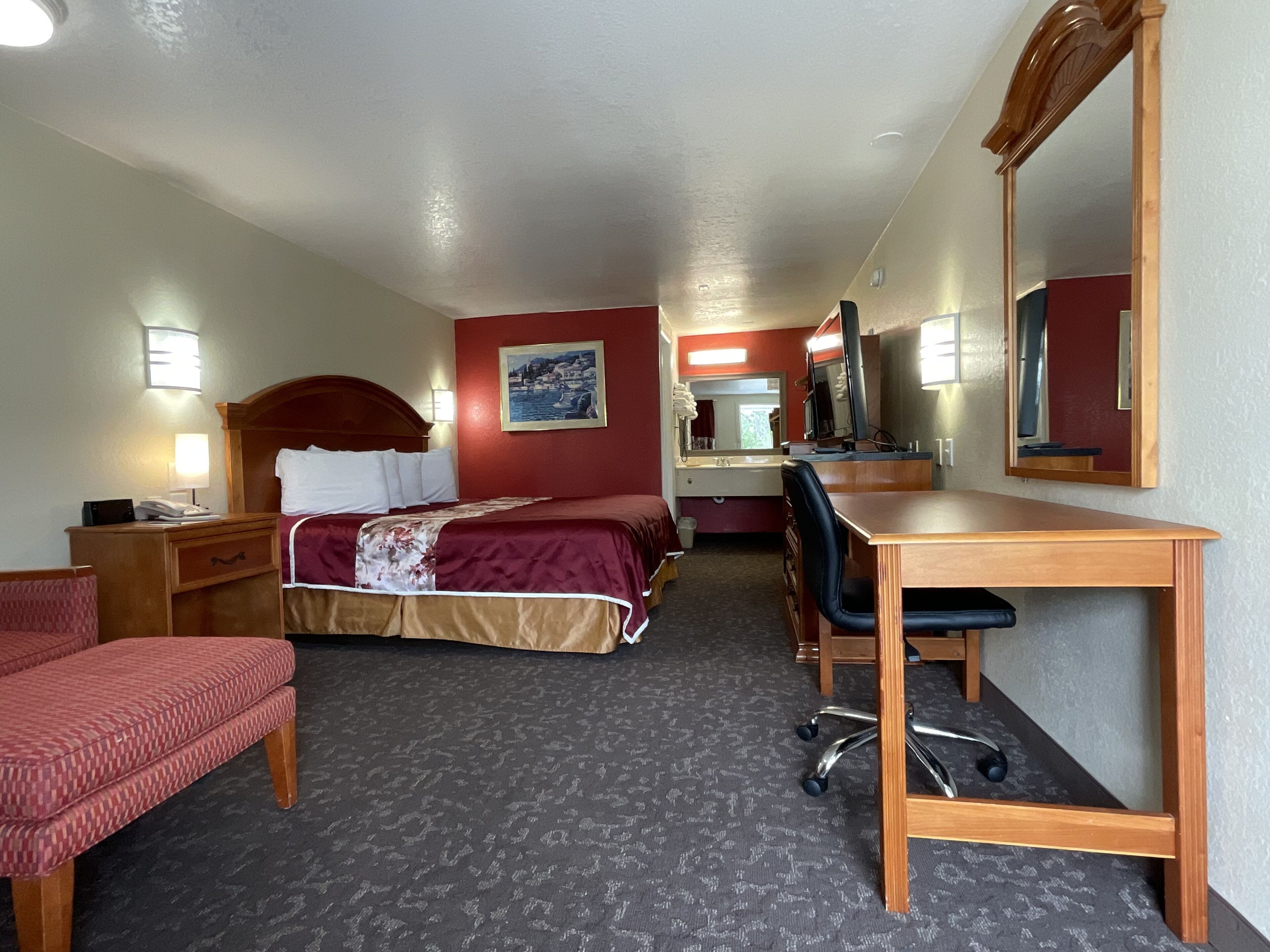 Una habitación de hotel con cama, escritorio, silla y un espejo grande.