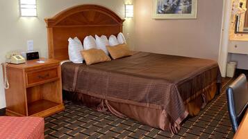Habitación de hotel con una cama grande, una mesita de noche de madera con un teléfono, un escritorio con una silla y un cuadro en la pared.