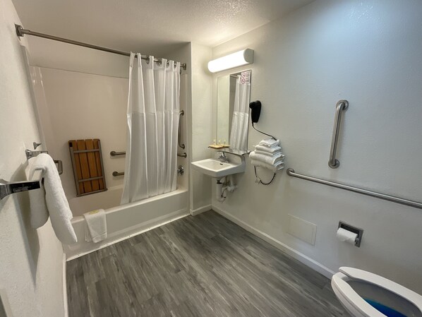 Un baño moderno con ducha, inodoro, lavamanos y barras de apoyo.