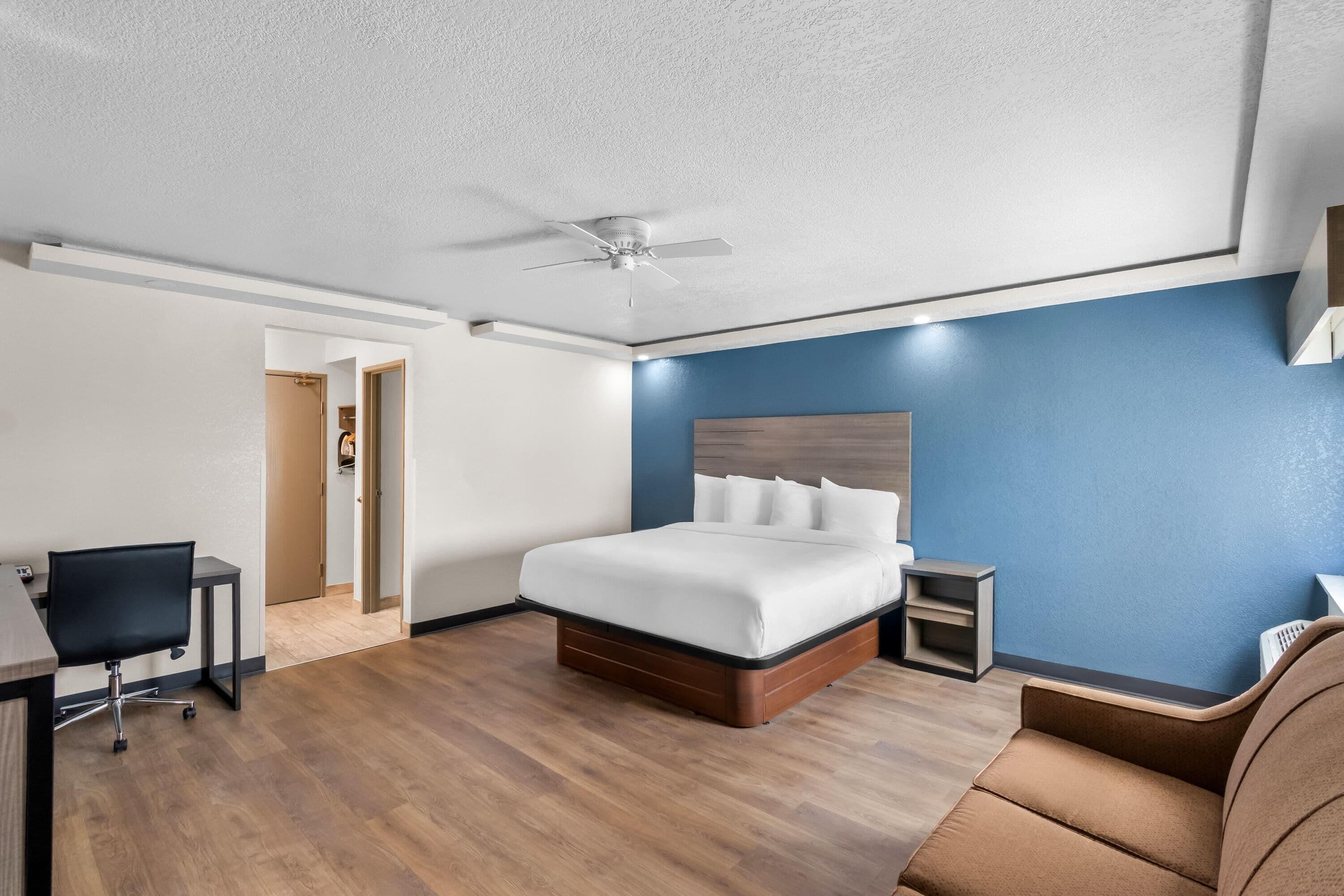 A hotel room with a bed, a desk, a chair, and a ceiling fan.
