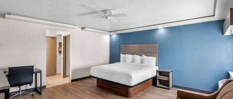 A hotel room with a bed, a desk, a chair, and a ceiling fan.
