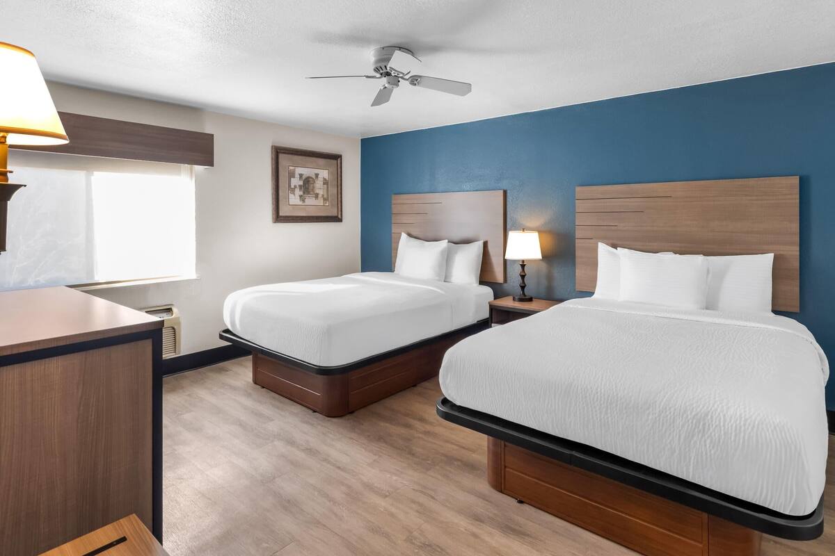 Una habitación de hotel con dos camas, un escritorio, un ventilador de techo y una ventana.