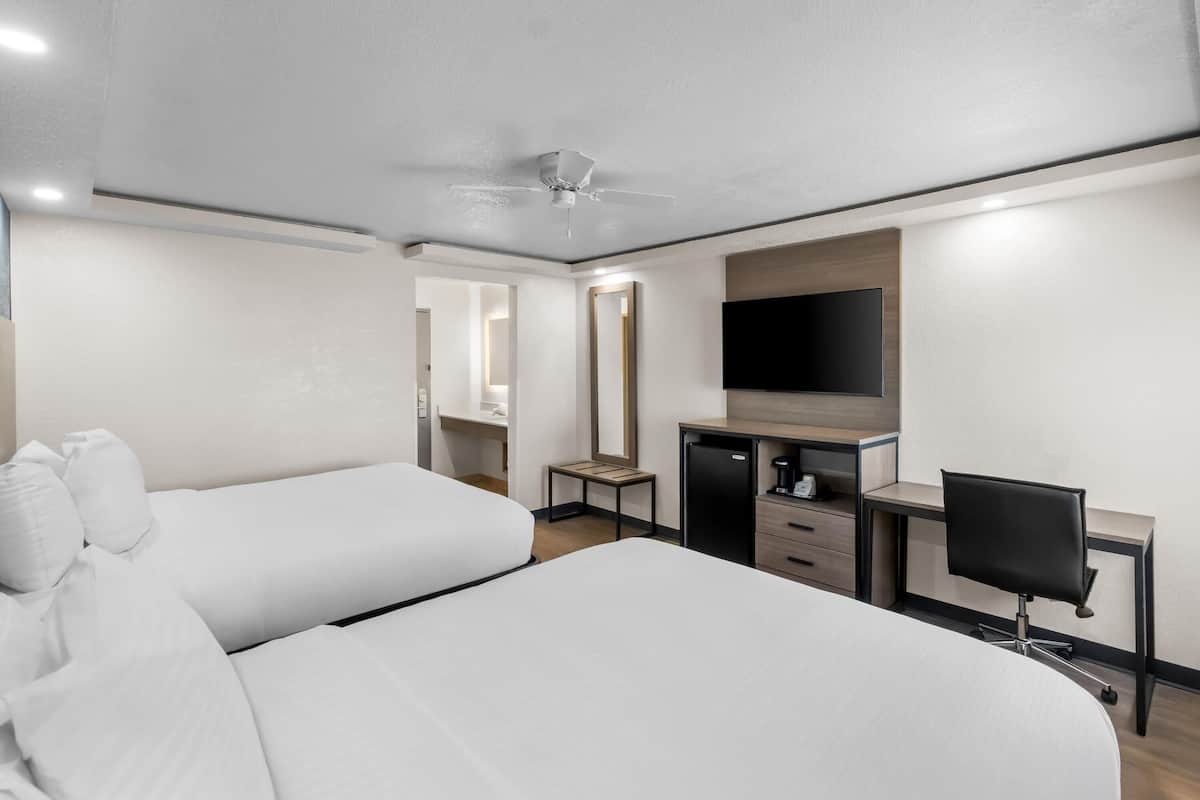 Habitación de hotel con dos camas, un escritorio, una silla, un televisor y un ventilador de techo.