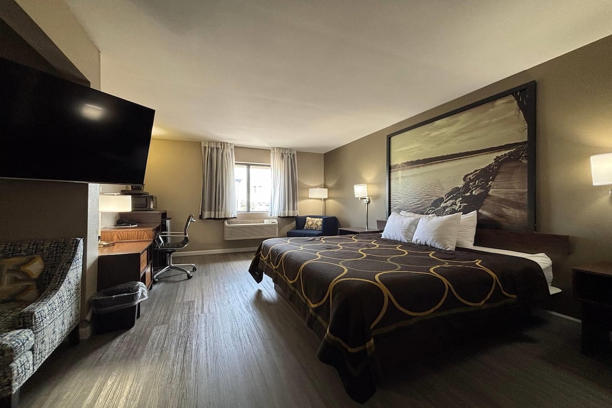 A hotel room with a large bed, a desk with a computer, a TV, and a window with curtains.