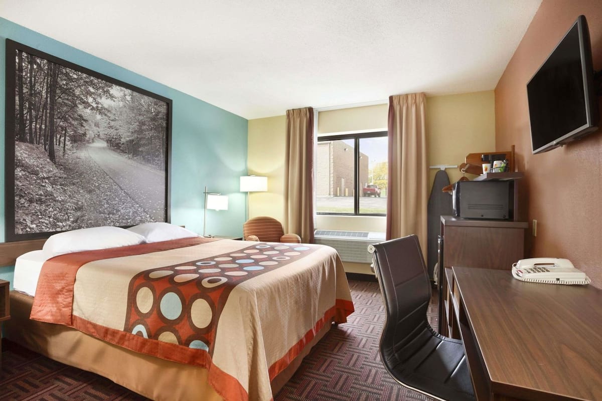 A hotel room with a bed, desk, chair, TV, and a large window.