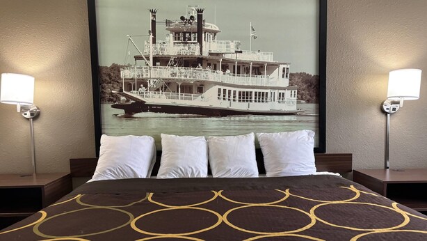 Habitación de hotel con cama, dos mesitas de noche y un cuadro grande con un barco de vapor en la pared.