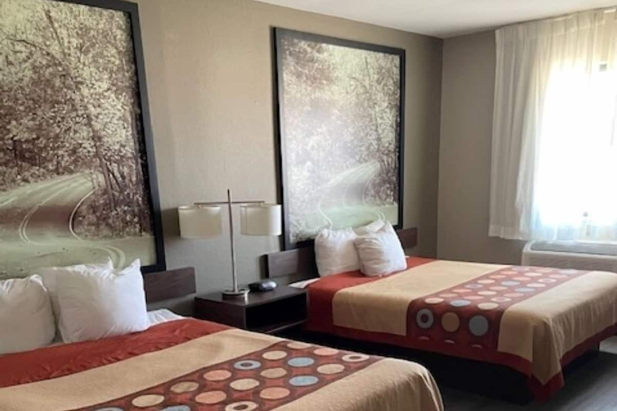 A hotel room with two beds, each with a patterned bedspread, a nightstand, a lamp, and two large wall art pieces.